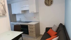 Ein kompakter Wohnbereich mit Küchenzeile, Essbereich und einer Couch mit Kissen.
