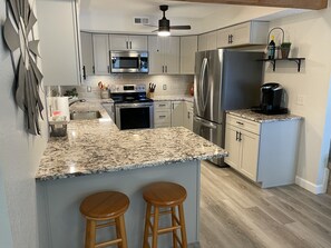 A modern kitchen with granite countertops, stainless steel appliances, and wooden stools.