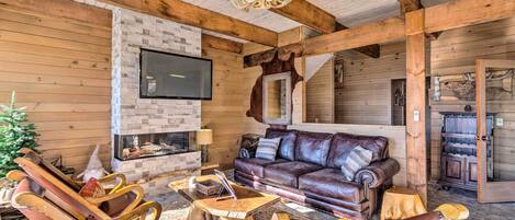 A cozy log cabin interior with a leather sofa, wooden rocking chairs, and a fireplace.