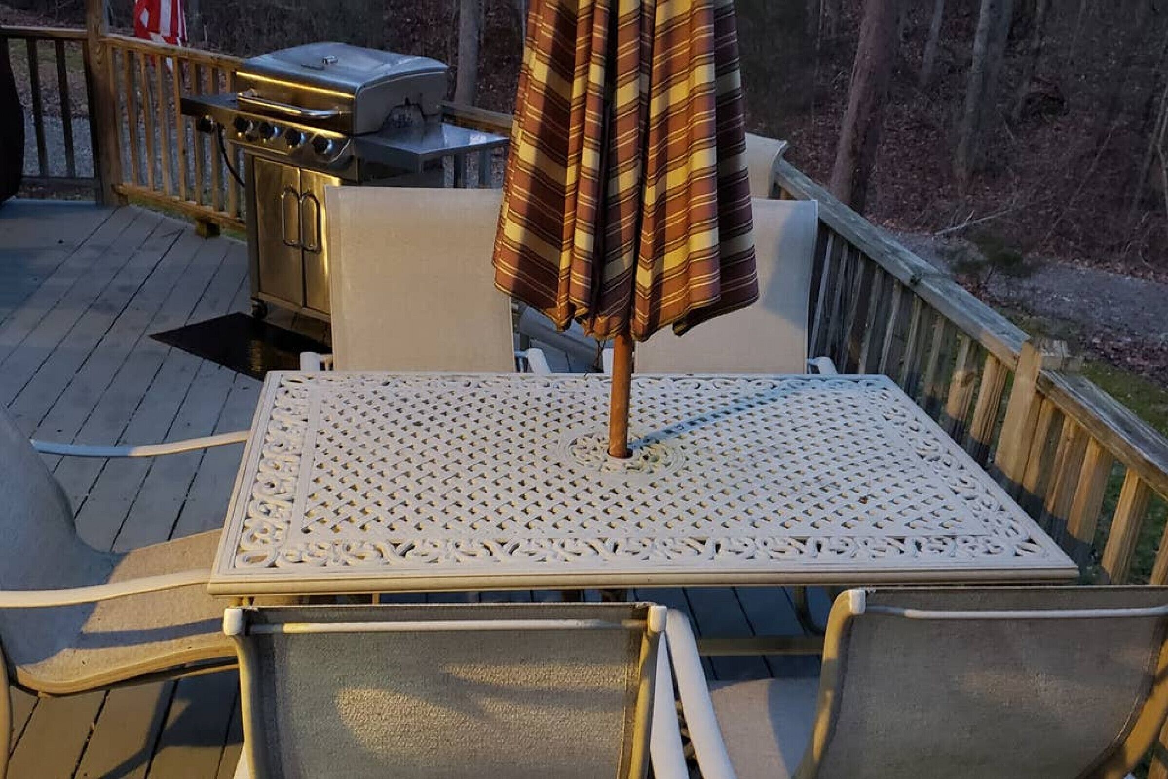 A deck with a white metal table and chairs, a grill, and a striped umbrella.