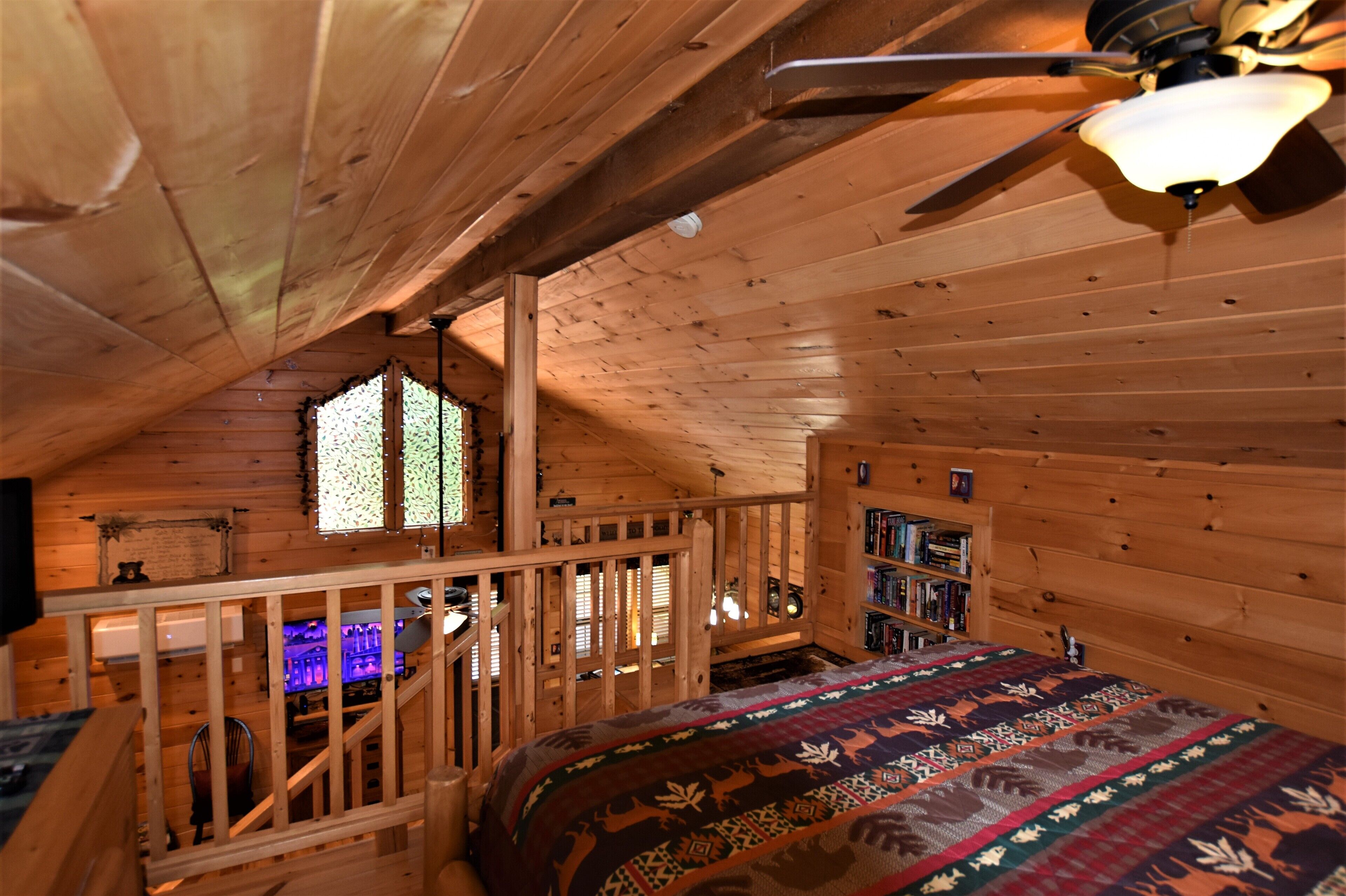 A wooden cabin with a loft bedroom, a bookshelf, and a window with blinds.