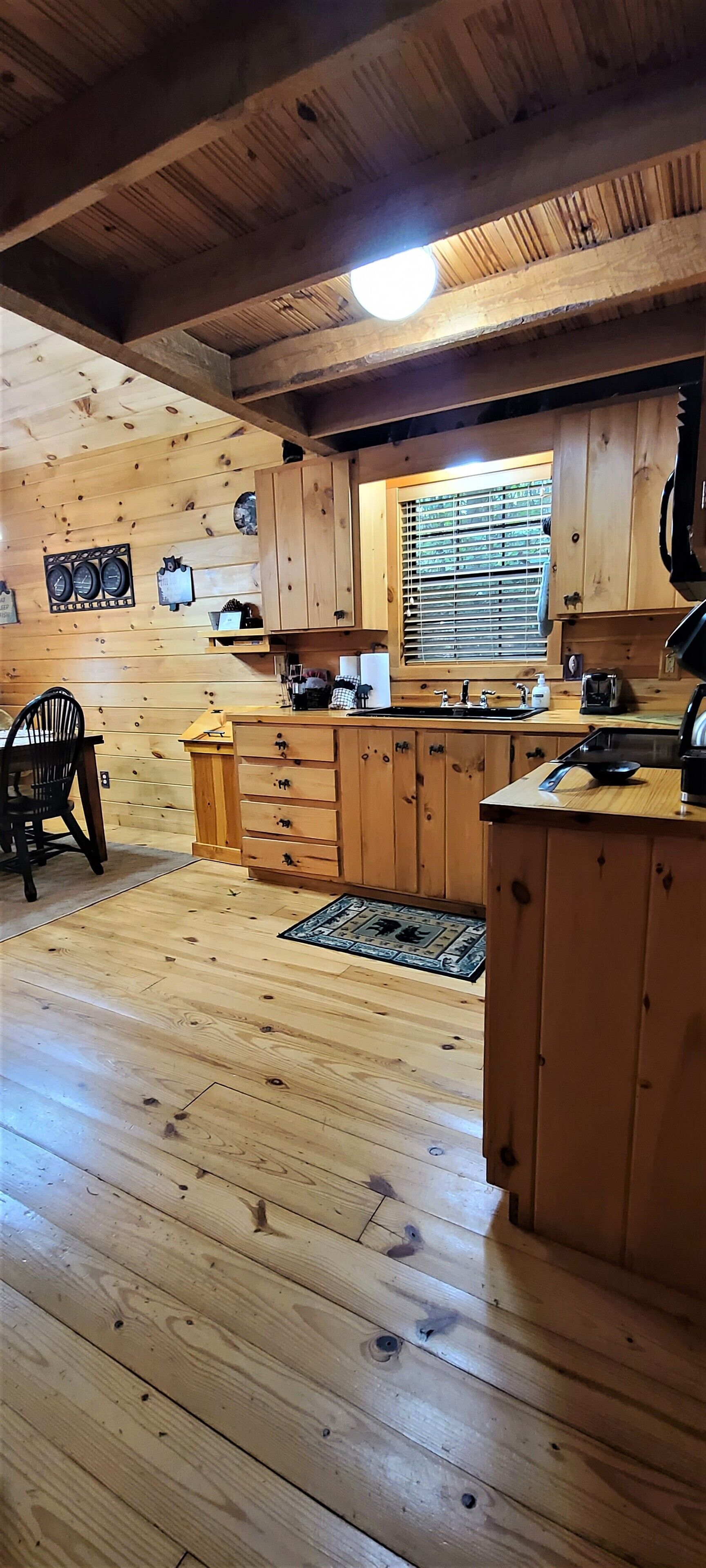 L’intérieur d’un chalet en bois comprend un coin cuisine avec des meubles de rangement en bois, une table à manger et une fenêtre équipée de stores.