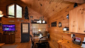 Ein gemütliches Blockhäuschen im Inneren mit Holzwänden, einem Essbereich mit Tisch und Stühlen, einem Fernseher und einem Weihnachtsbaum.