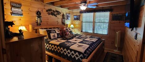 A cozy cabin bedroom with a wooden bed, a ceiling fan, and a window with blinds.