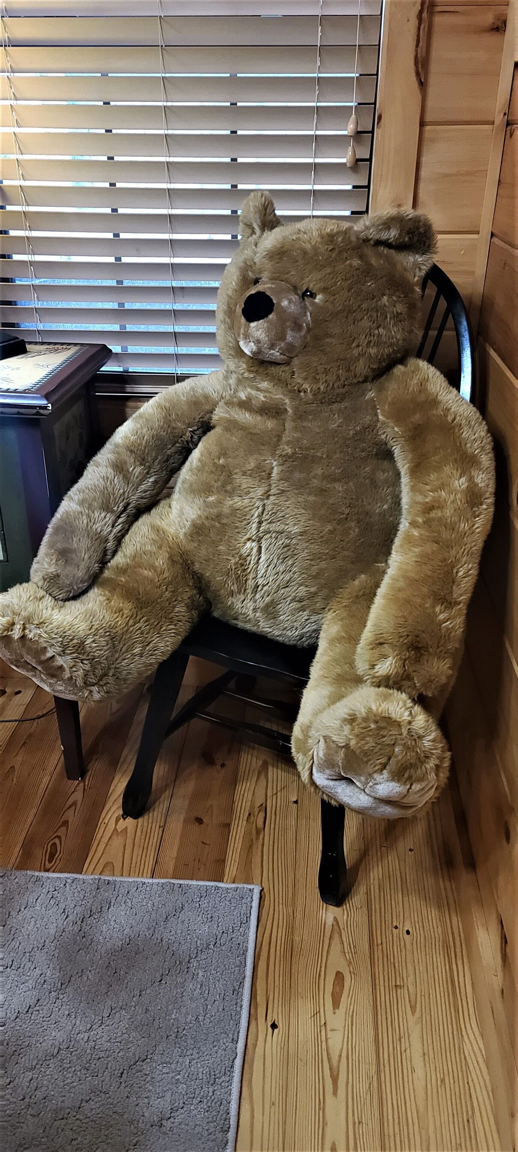 Ein großer Teddybär sitzt auf einem hölzernen Stuhl.