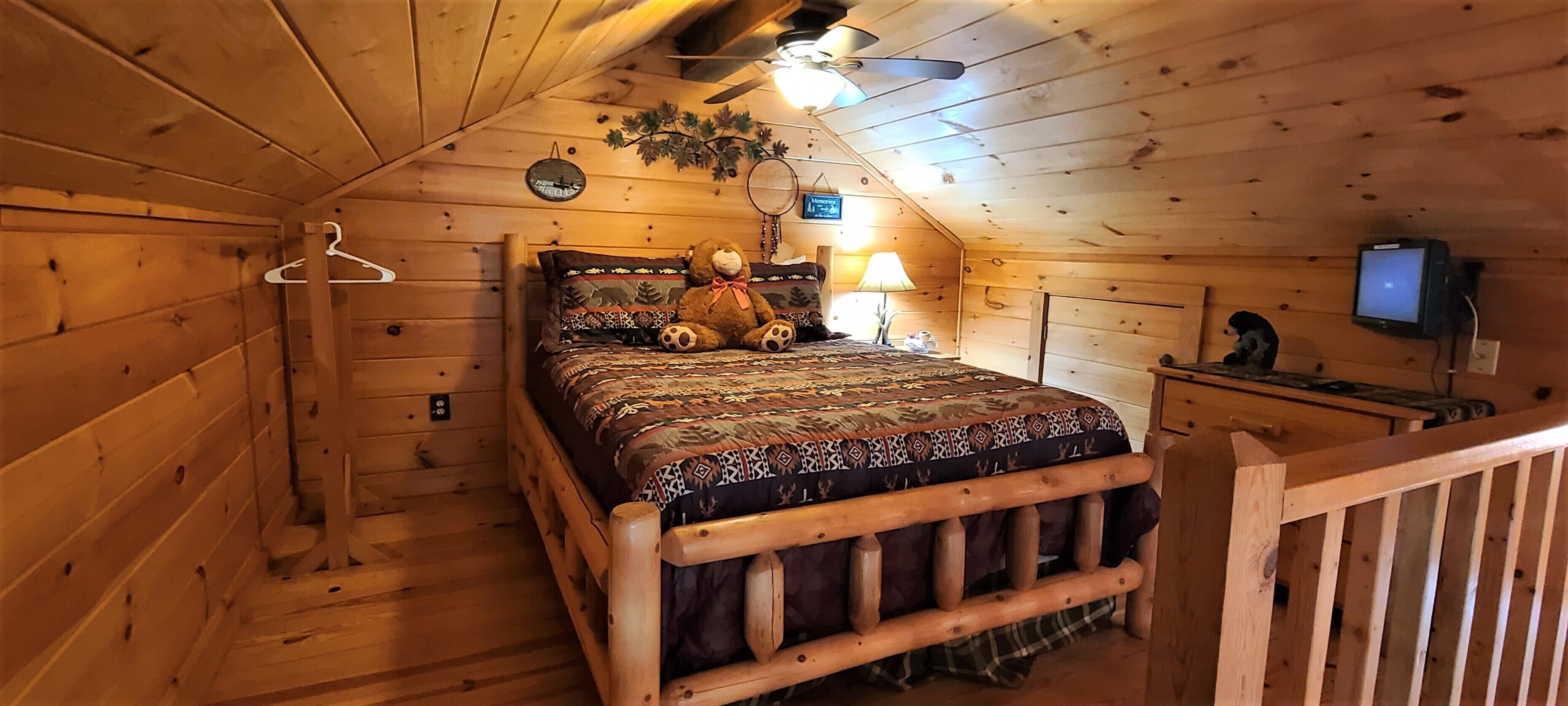 A cozy wooden cabin bedroom with a bed, a hanging clothes rack, a lamp, and a television.