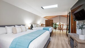 Una camera d'albergo moderna con due letti grandi, un'area pranzo e una televisione a parete.