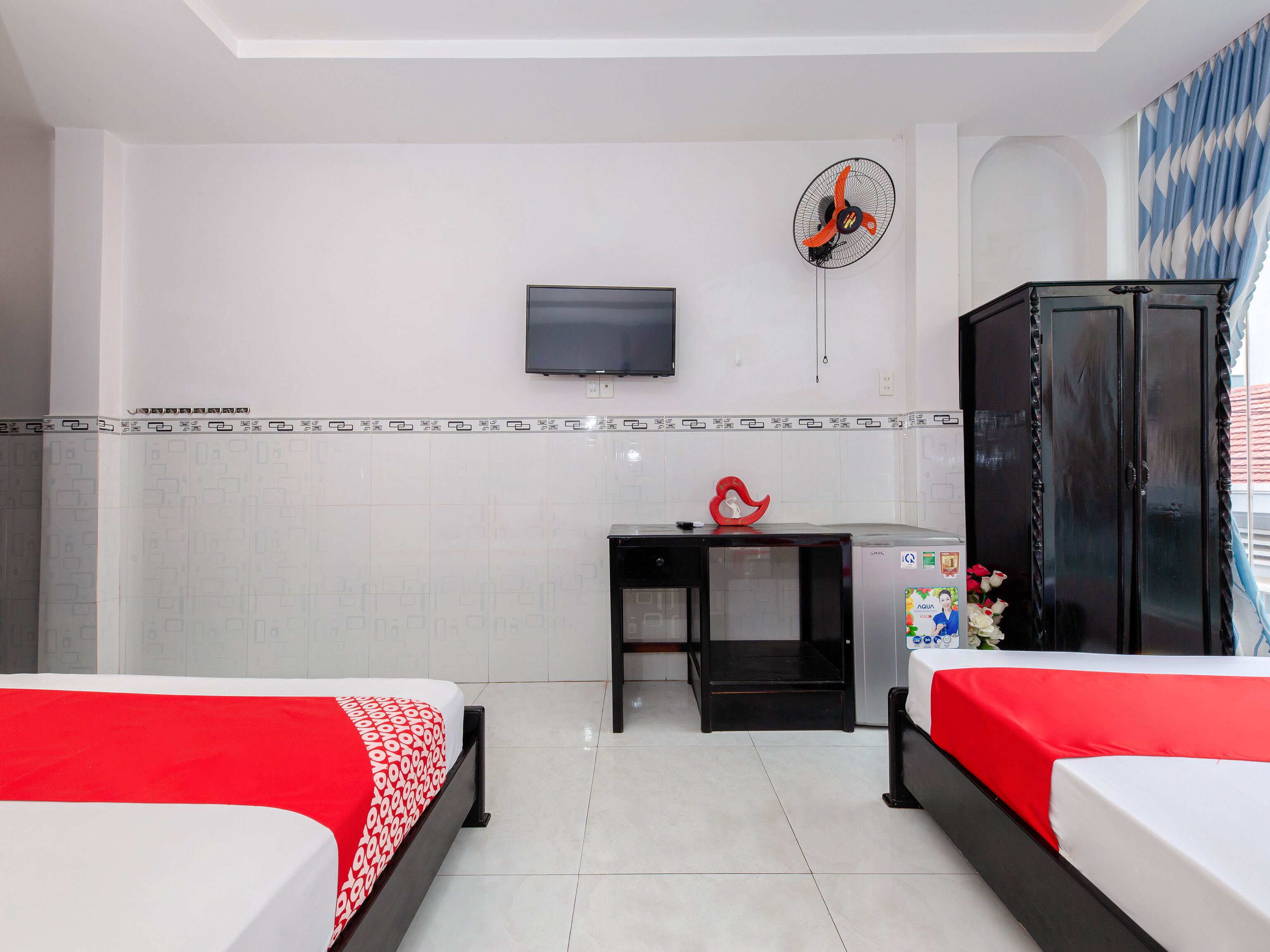 A hotel room with two beds, a TV, a desk, a wardrobe, and a fan.