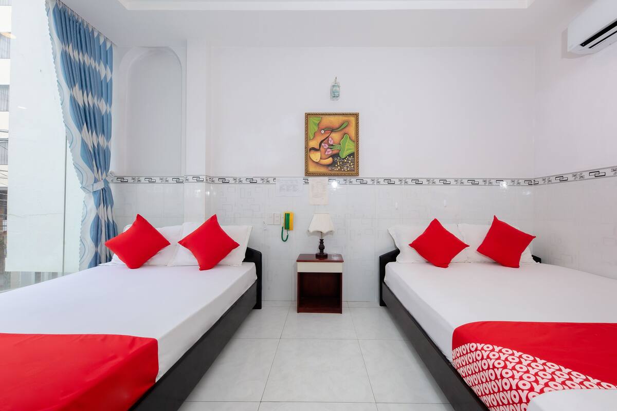 Une chambre d’hôtel avec deux lits, chacun agrémenté de draps rouges et blancs, une petite table de chevet avec une lampe, un téléphone fixé au mur et un tableau décoratif au-dessus des lits.