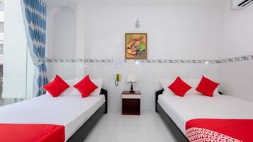 Una camera d'albergo con due letti, entrambi con biancheria rossa e bianca, un comodino con una lampada, un telefono fissato al muro e un quadro decorativo sopra i letti.