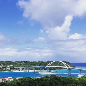 A large white bridge spanning a body of water with a beach and greenery in the background. - Churaumi Kafuu Terrace (Motobu)