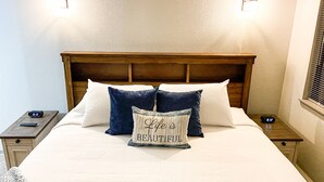 A neatly made bed with a wooden headboard, two bedside tables with clocks, and a wall-mounted light fixture. - Ski-In Ski-Out Brian Head Giant Steps Condo (Brian Head)