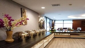 A modern hotel reception area with a long counter, a vase of flowers, and a large window providing natural light. - Hotel Zia Sanno Jakarta - Pluit (Jakarta)