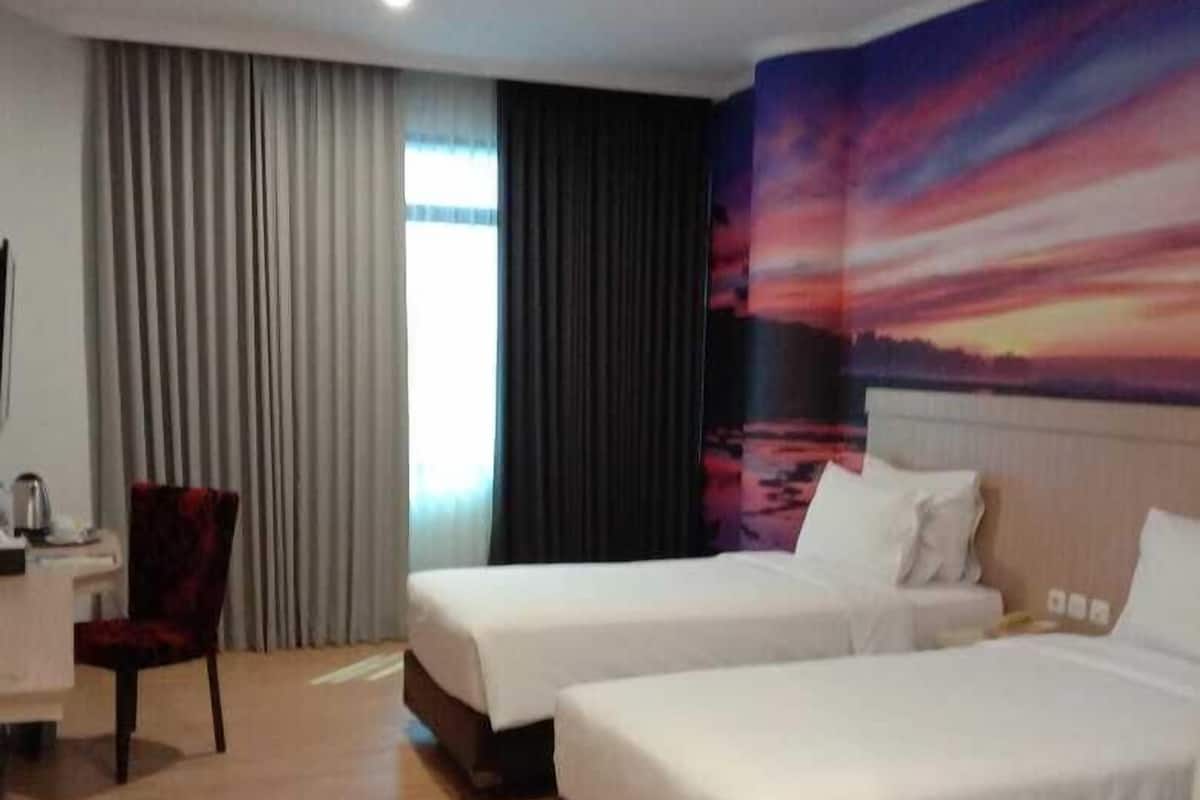 A hotel room with two beds, a desk, a chair, and a large window with curtains.