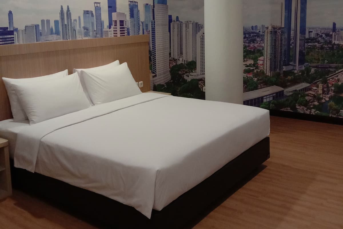 A hotel room with a bed, wooden headboard, and a cityscape mural on the wall.