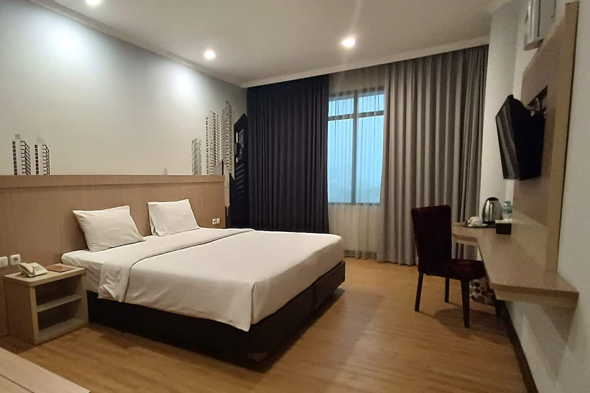 A hotel room with a large bed, a bedside table with a phone, a chair, a small table with a kettle, and a TV mounted on the wall.