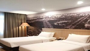 A hotel room with two beds, a cityscape mural, a lamp, and a view of the city. - Hotel Zia Sanno Jakarta - Pluit (Jakarta)