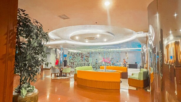 A spacious lobby with a central reception desk, a large potted plant, and a polished floor. - Hotel Zia Sanno Jakarta - Pluit (Jakarta)