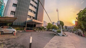 A modern hotel with a curved facade, a visible entrance, and a parking area with several cars. - Hotel Zia Sanno Jakarta - Pluit (Jakarta)