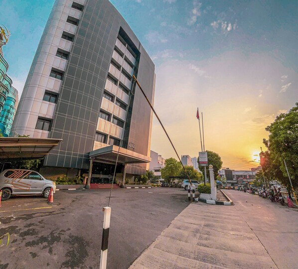 Un hotel moderno con fachada curva, entrada visible y un estacionamiento con varios coches.