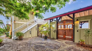 A two-story building with a staircase leading to a balcony, a wooden door, and a stone-paved courtyard with potted plants. - The “Promise Tree” is a great family  gathering place in Kailua Kona! (Kailua-Kona)