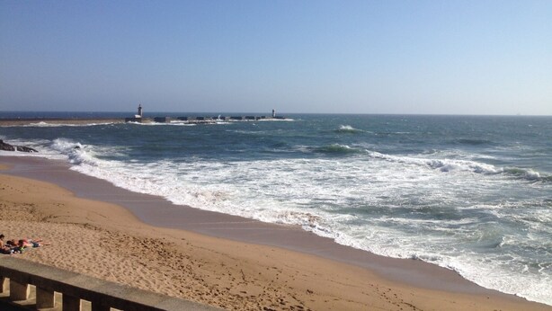 A beach with waves, a pier, and a lighthouse.