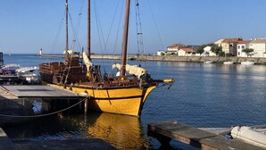 A yellow boat docked at a marina with a clear view of the sea and buildings in the background.
