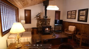 A cozy living room with a stone fireplace, a television, and wooden furniture. - River Ranch Log home 3 BR 2 bath on the river porches ATV drive-in/out (Lake City)