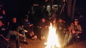 Een groep mensen zit 's nachts rond een kampvuur.