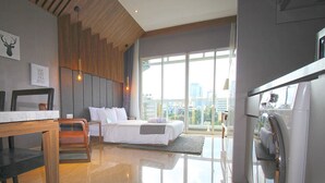 Una habitación de hotel moderna con cama, mesa de comedor, sillas, zona de cocina y grandes ventanales con vista a la ciudad.
