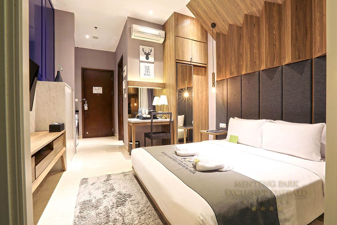 Une chambre d’hôtel avec un grand lit, un bureau avec une chaise, un miroir et une tête de lit en bois.