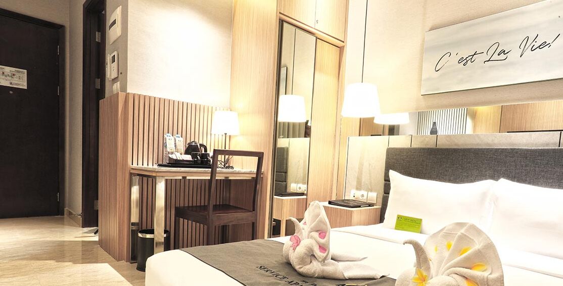 Una habitación de hotel con cama, mesita de noche, lámpara y un escritorio con silla.