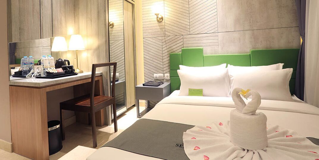Een hotelkamer met een bureau, stoel, bed en een handdoek gevouwen tot een zwaan.