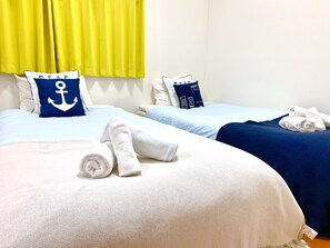 A hotel room with two beds, each with a different colored bedspread, pillows with anchor designs, and neatly folded towels. - Paragon Residence OSAKA (Osaka)