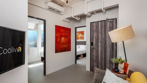 A modern office space with a large flat-screen TV, a sofa with cushions, and a lamp on a side table. - Cooliv Waterfront (Singapore)
