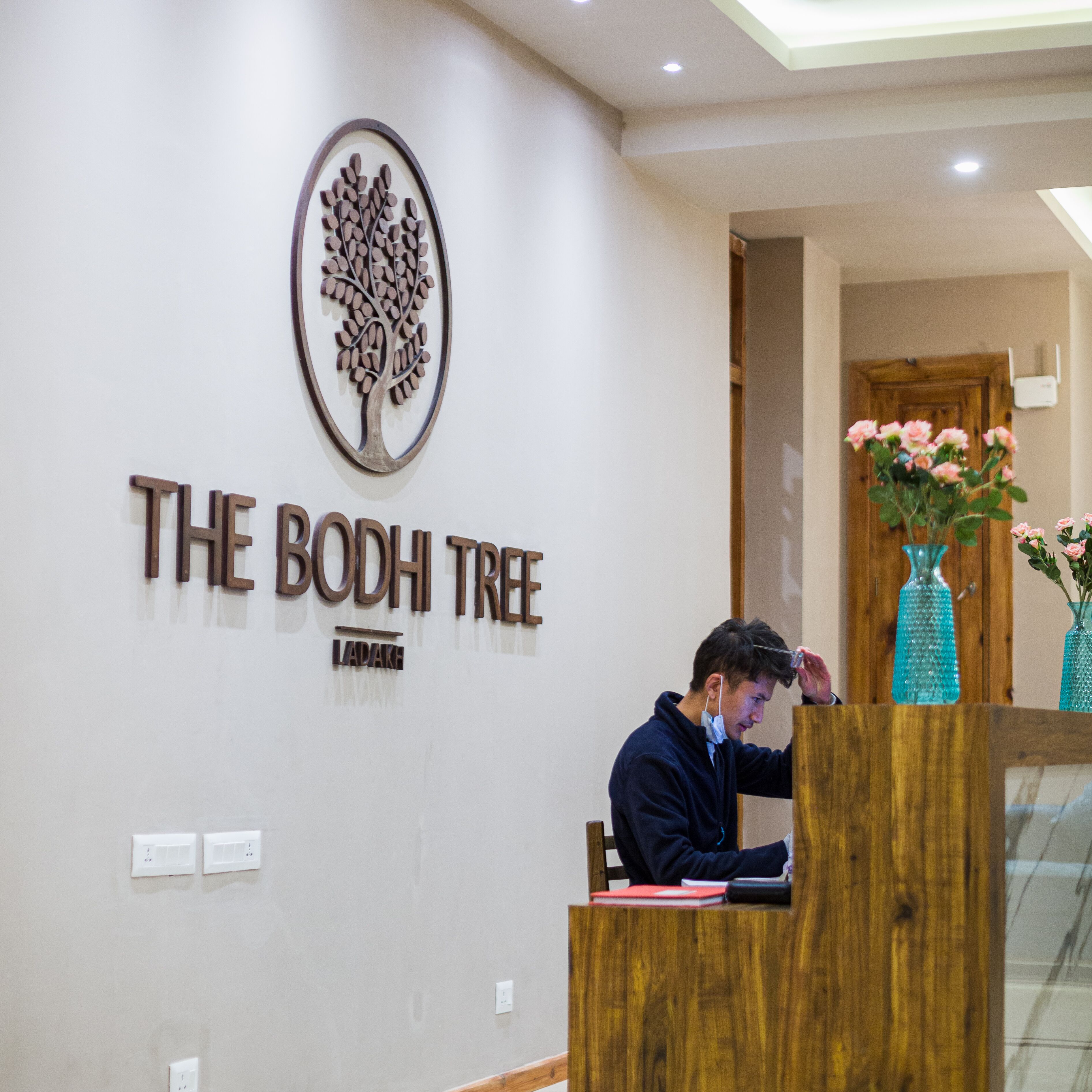 En receptionsdisk med træfinish, et logo af et træ og teksten 'THE BODHI TREE' på væggen.