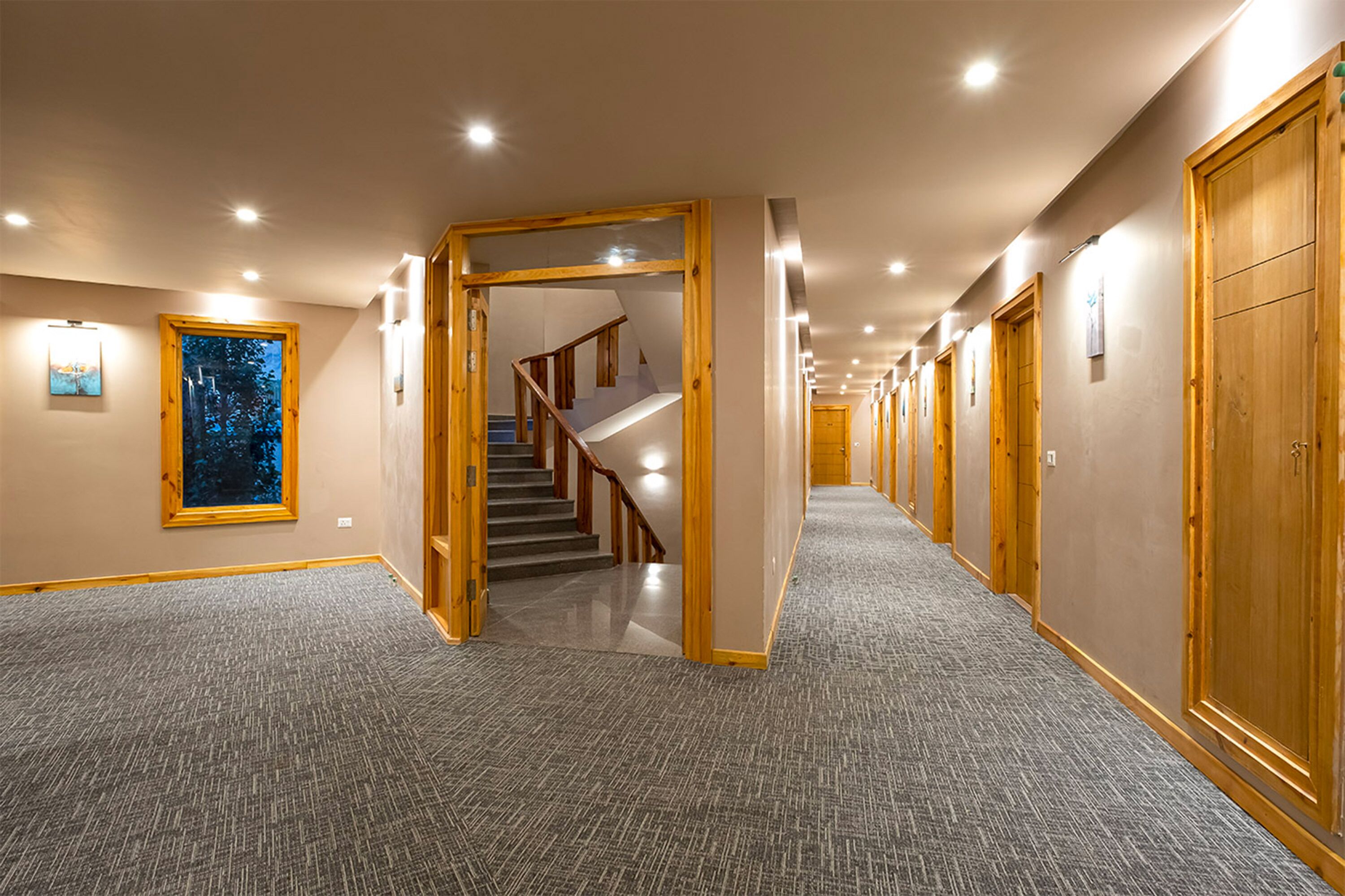 A hotel hallway with carpeted floors, wooden doors, and a staircase leading to another floor.