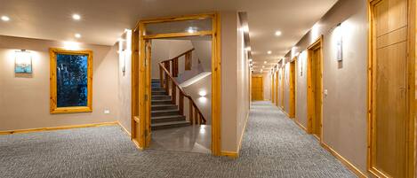 A hotel hallway with carpeted floors, wooden doors, and a staircase leading to another floor.