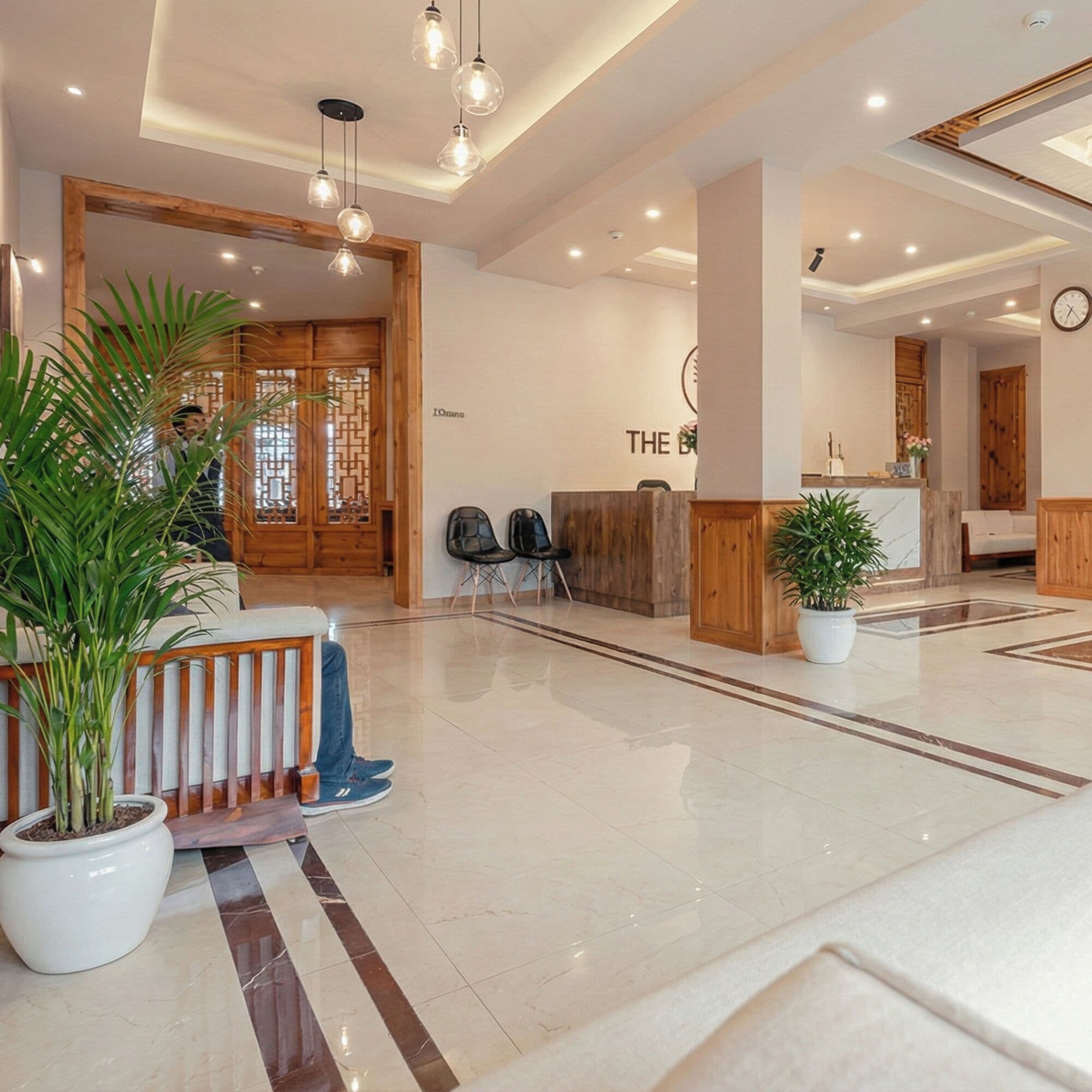 Een moderne hotellobby met een receptiebalie, een zithoek en potplanten.