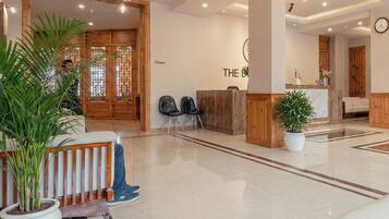 Een moderne hotellobby met een receptiebalie, een zithoek en potplanten.