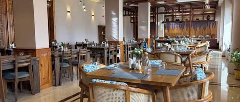 A restaurant with wooden tables and chairs, a tiled floor, and hanging light fixtures.