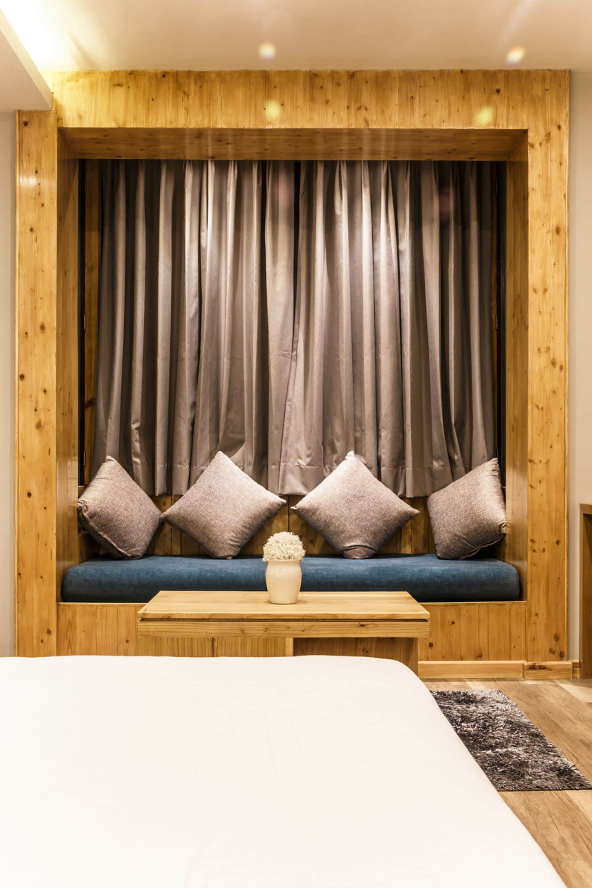 A room with a wooden headboard, a blue sofa with cushions, and a small table with a vase.