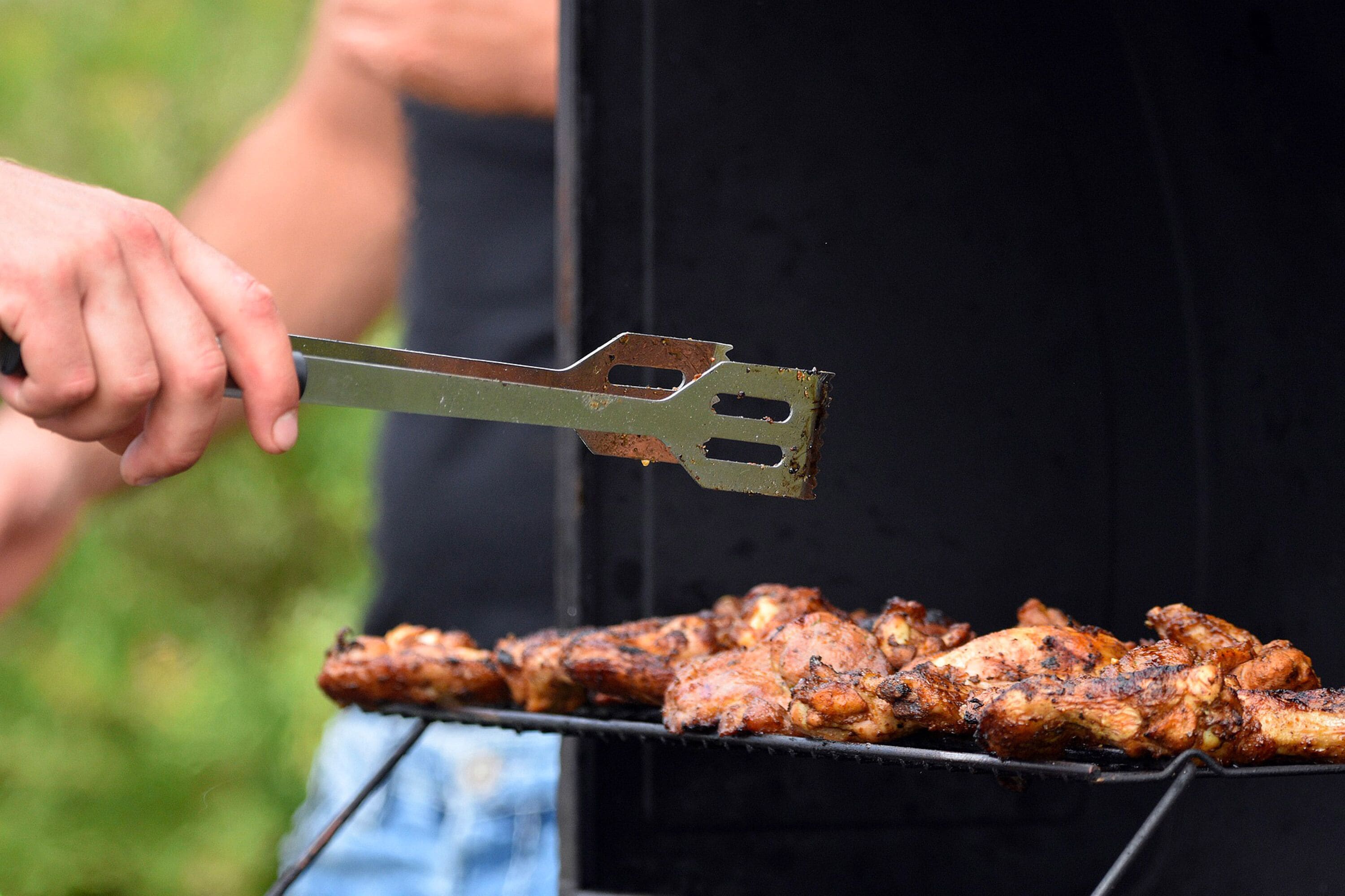 A person grilling chicken on an outdoor grill.
