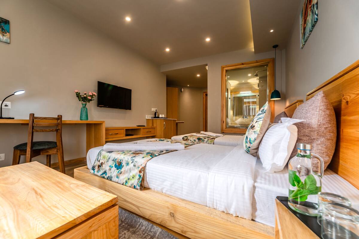 Quarto de hotel moderno com cama de madeira, uma mesa, uma cadeira e uma TV na parede.