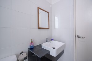 A bathroom with white tiles, a white sink, a mirror, and a door.