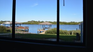 A lakeside view from a window, featuring a dock with a gazebo, a wooden deck, and a small building with a covered area. - "Water's Edge" Beautiful Waterfront Home In Edgewater, Florida (Edgewater)