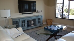 A living room with a television mounted on the wall, a blue cabinet with glass doors, a glass coffee table, and a white sofa. - "Water's Edge" Beautiful Waterfront Home In Edgewater, Florida (Edgewater)