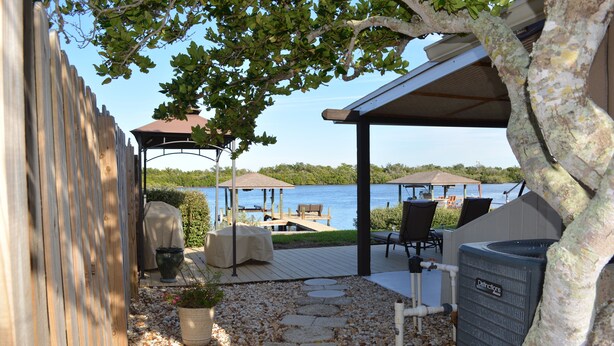 A covered outdoor patio with a view of a lake, stone steps, outdoor furniture, and a water heater. - "Water's Edge" Beautiful Waterfront Home In Edgewater, Florida (Edgewater)