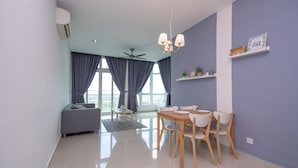 A modern living room with a dining area, large windows, and a ceiling fan. - OYO Home 89736 Unbelievable 2br 1medini (Iskandar Puteri)