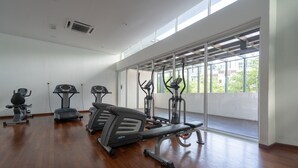 A spacious gym with treadmills, elliptical machines, and a bench. Large windows provide natural light and a view of greenery outside. - OYO Home 89736 Unbelievable 2br 1medini (Iskandar Puteri)